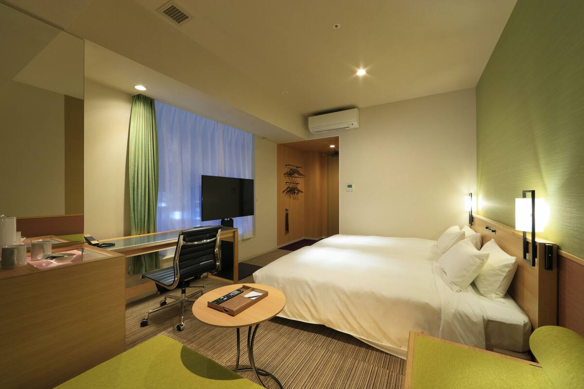 A hotel room with a bed, desk, chair, and a small table.