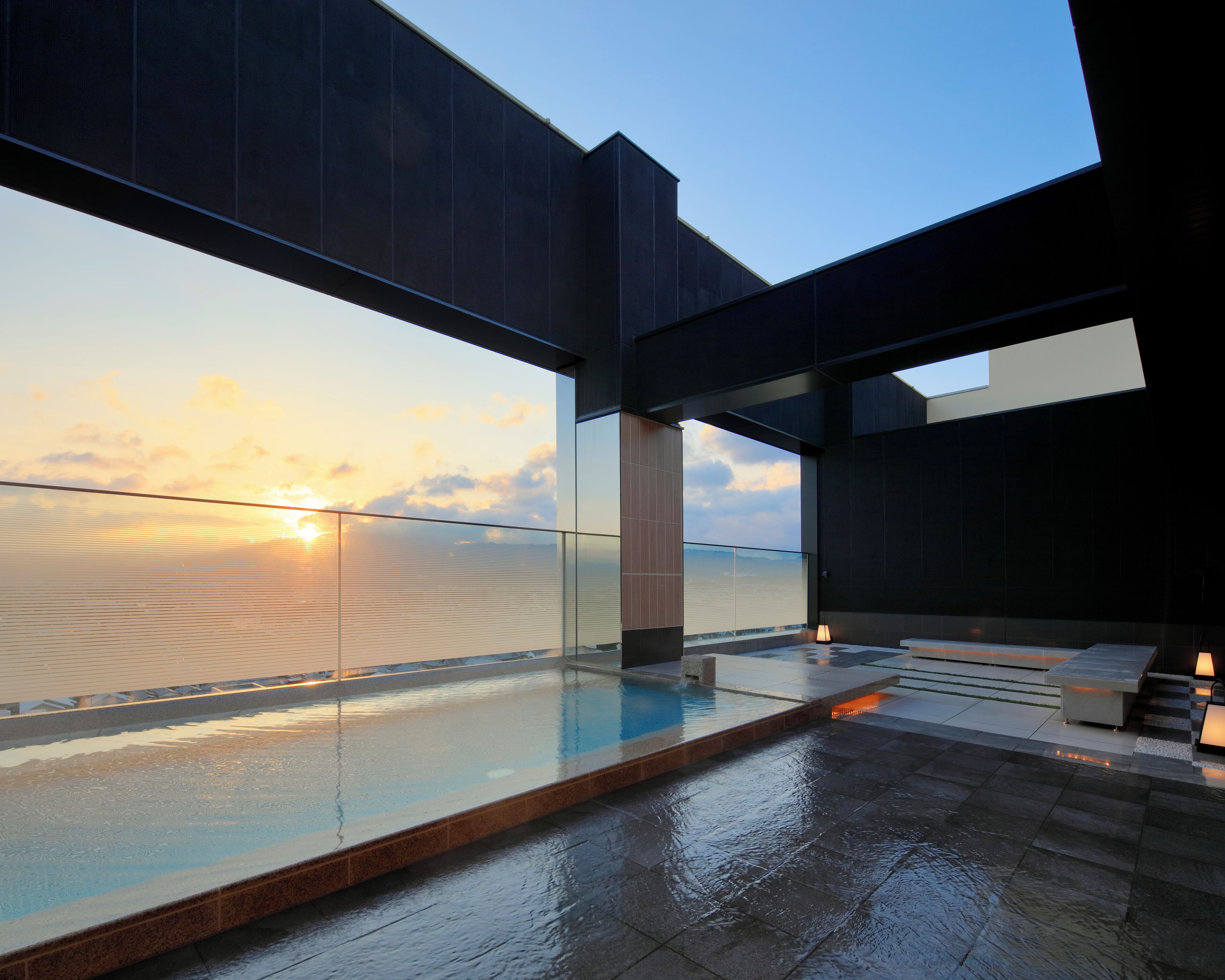 A modern building with a glass pool reflecting the sunset, large windows, and a clear sky.