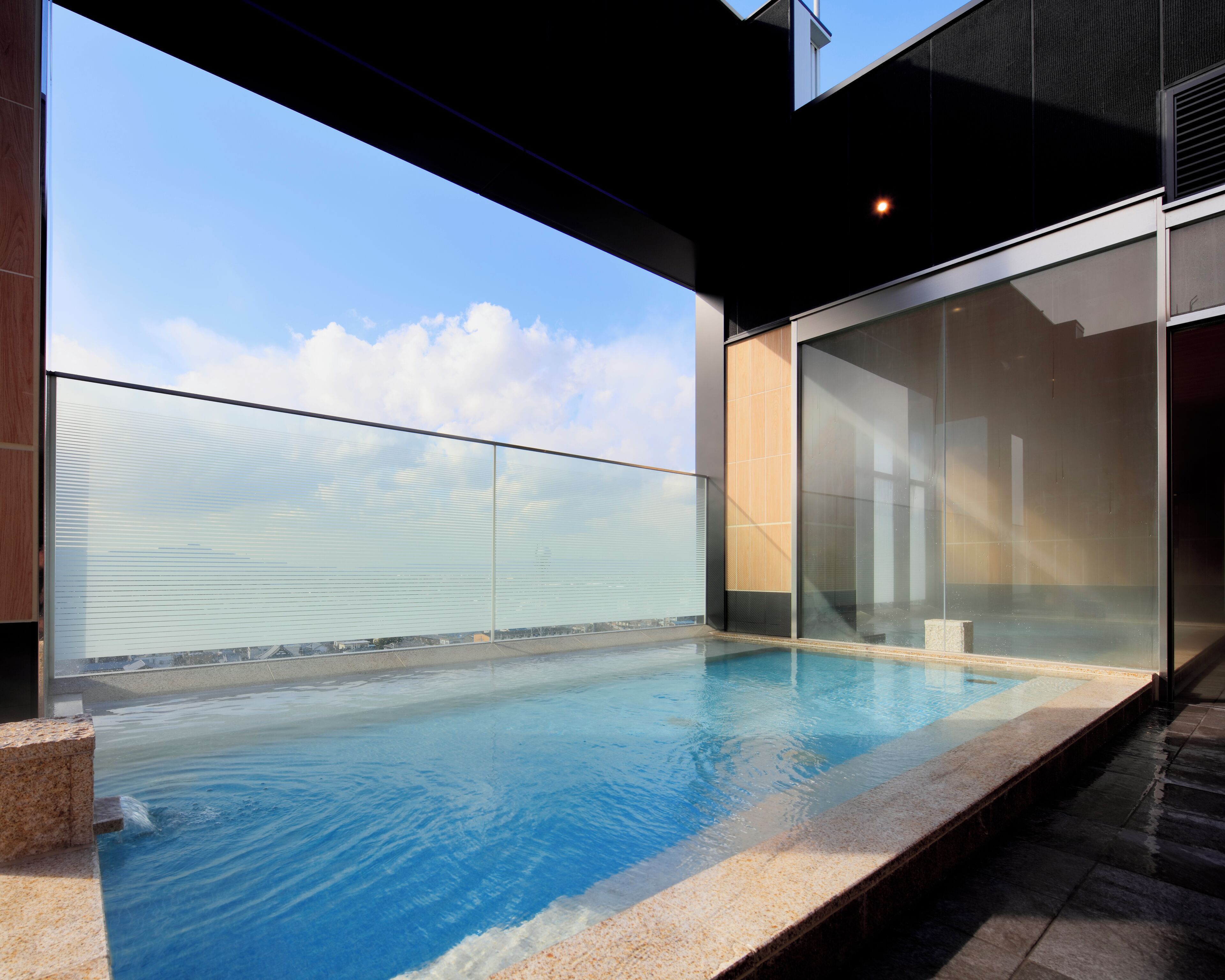 Ein moderner Pool im Freien mit Glastrennwand, blauem Himmel und Blick auf die Stadt.
