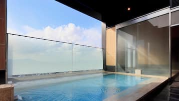 Ein moderner Pool im Freien mit Glastrennwand, blauem Himmel und Blick auf die Stadt.