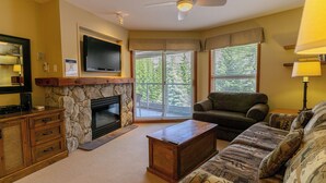 Ein Wohnzimmer mit Kamin aus Stein, einem flachbildfernseher, der darüber angebracht ist, einer Couch, einem Couchtisch und einem Fernseher auf einem Holzkabinett.