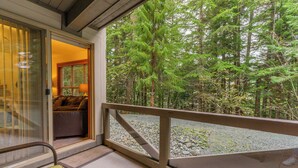 Una terraza de madera con un ventanal de vidrio que da a una habitación con un sofá y una lámpara.