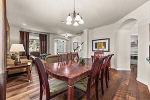 A spacious dining area with a wooden table and chairs, a sofa, and a lamp.