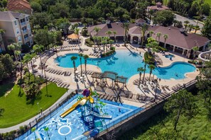 An aerial view of a resort with two large swimming pools, a water park, and surrounding palm trees.