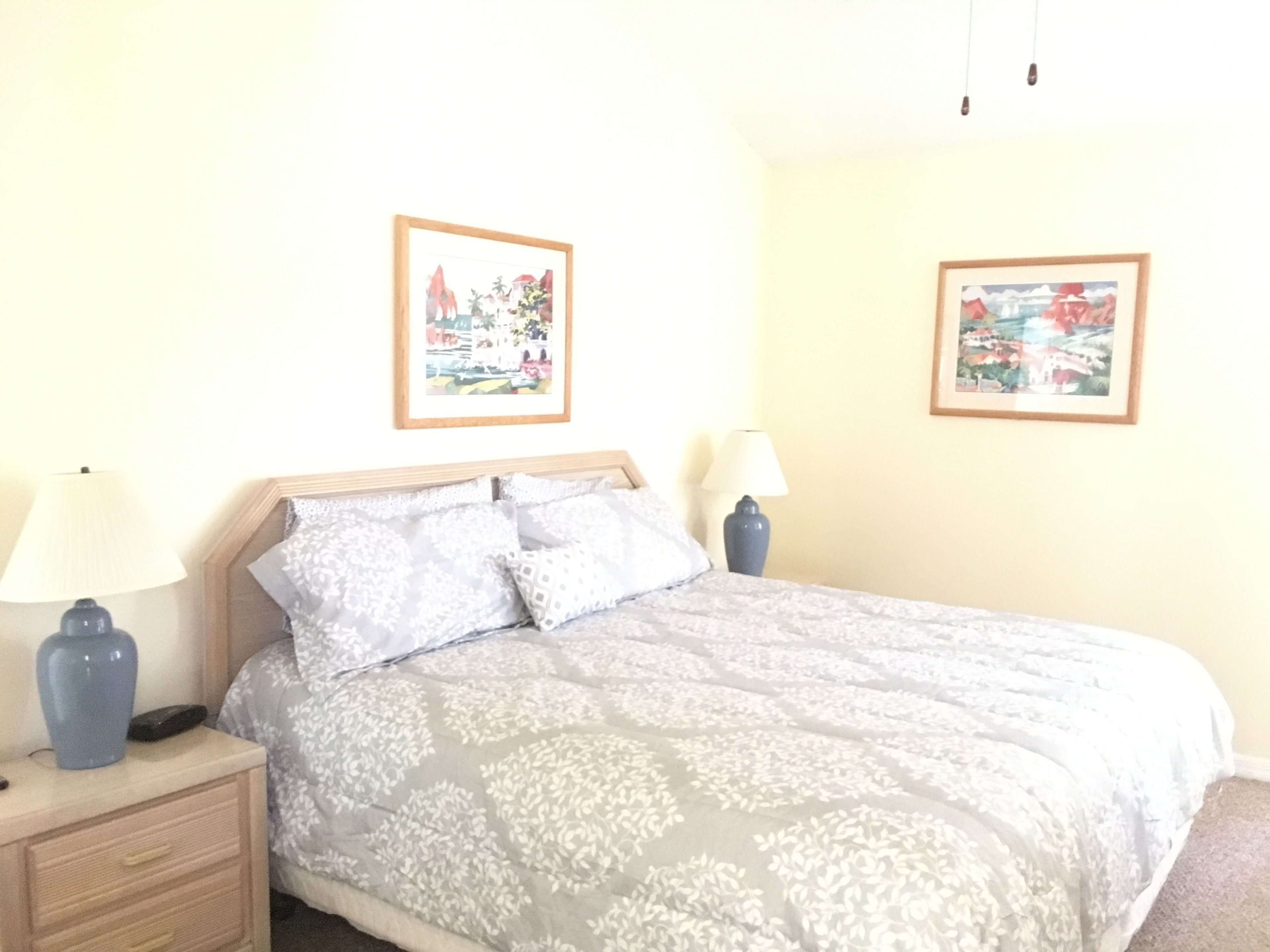 Een slaapkamer met een bed, twee bedlampen, een nachtkastje en twee ingelijste foto’s aan de muur.