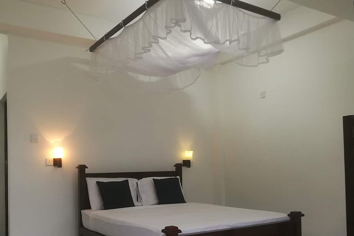 Cama de solteiro com estrutura de madeira e roupa de cama branca, duas luminárias fixadas na parede e teto com dossel branco.