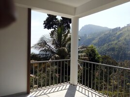 Un balcón con barandilla de metal, un pilar blanco y vistas a un paisaje montañoso con vegetación.