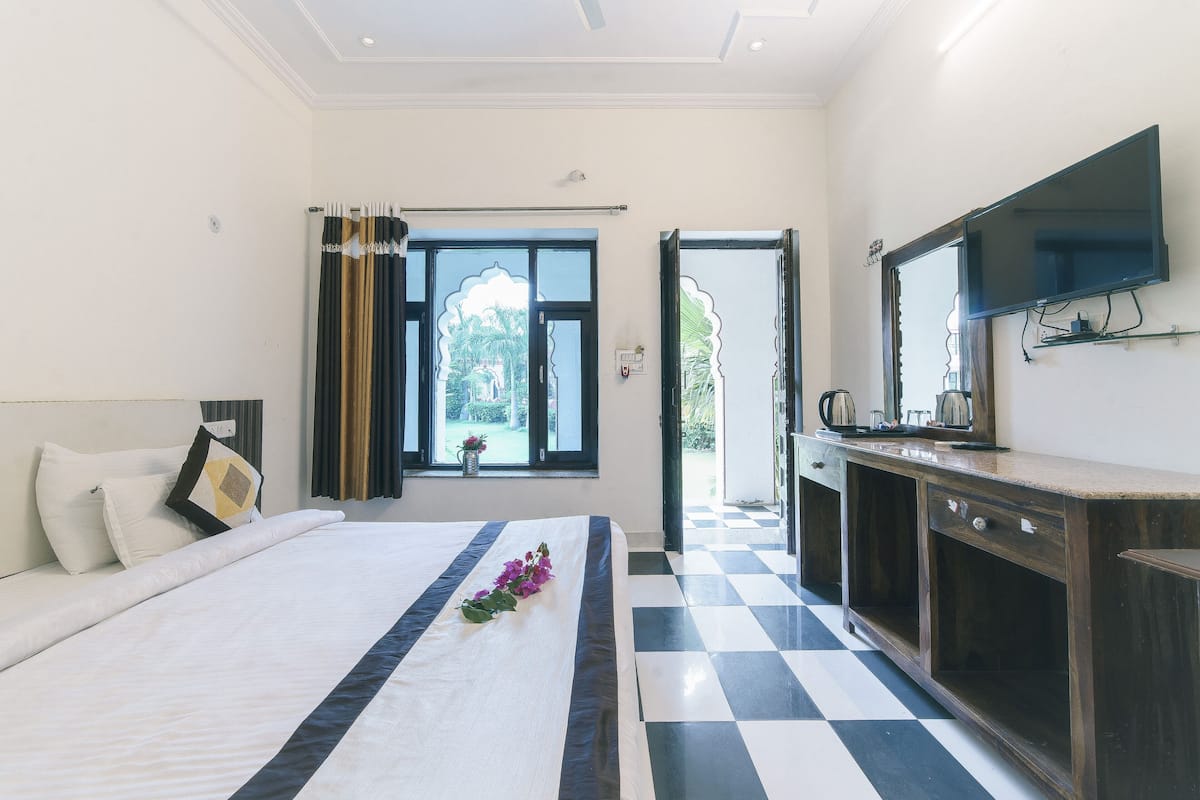 A hotel room with a bed, a bedside table, a mirror, a window with curtains, and a checkered floor.