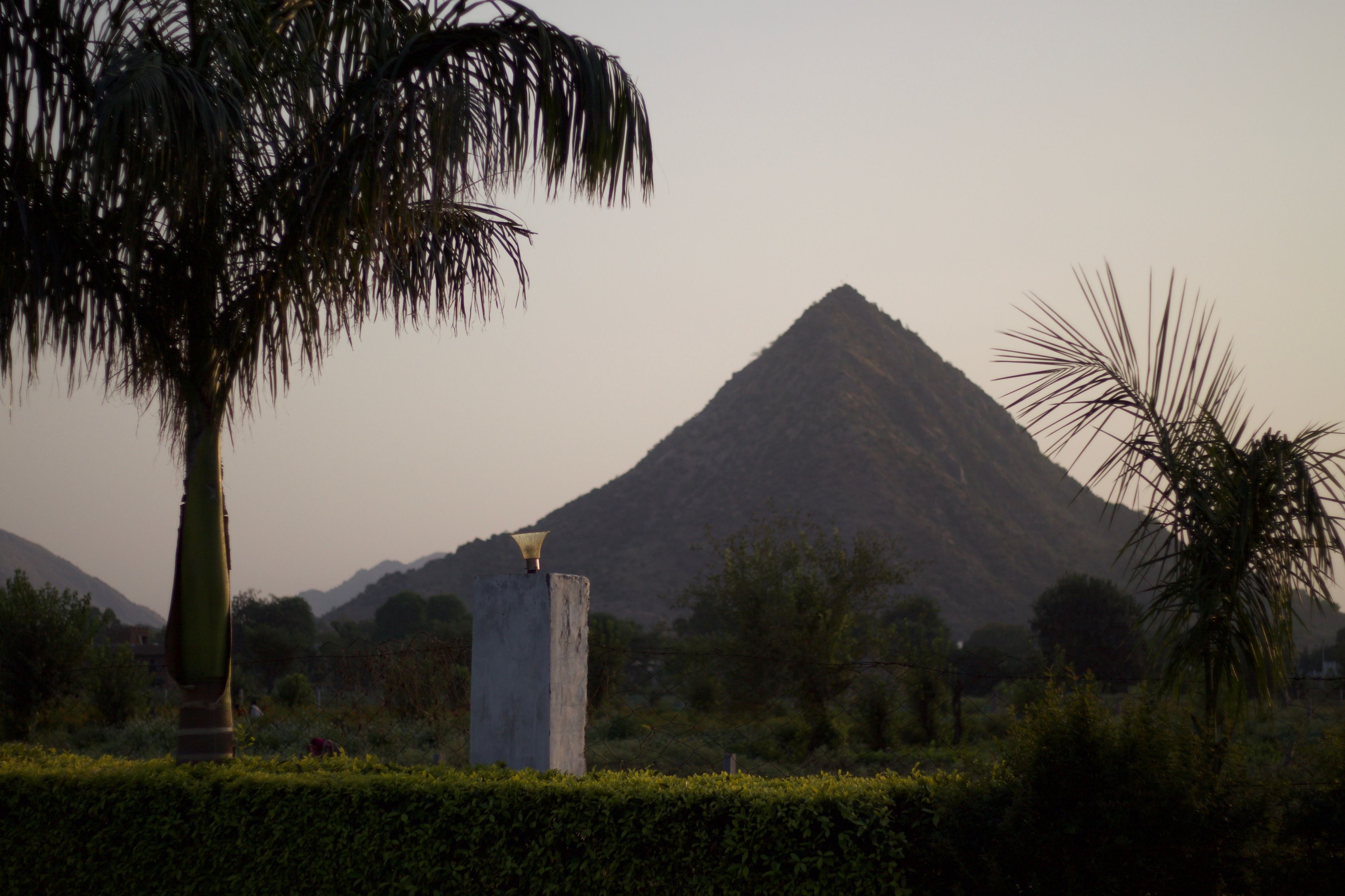 Montagna con struttura a forma di piramide sullo sfondo, circondata da vegetazione e una palma.