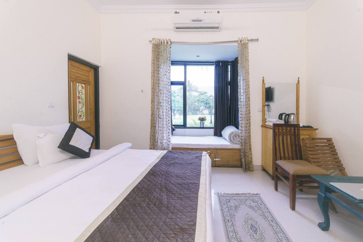 A hotel room with a bed, a window with curtains, a television, a desk, and a chair.