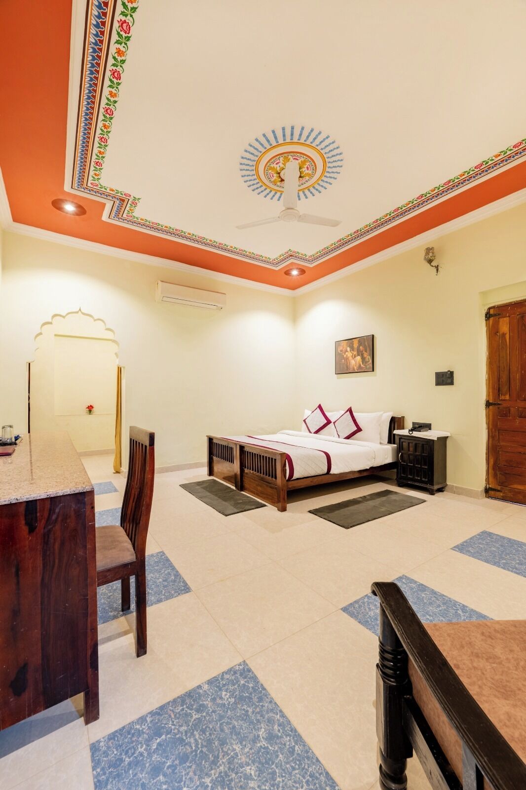 A hotel room with a bed, a desk, a chair, a ceiling fan, and a door.