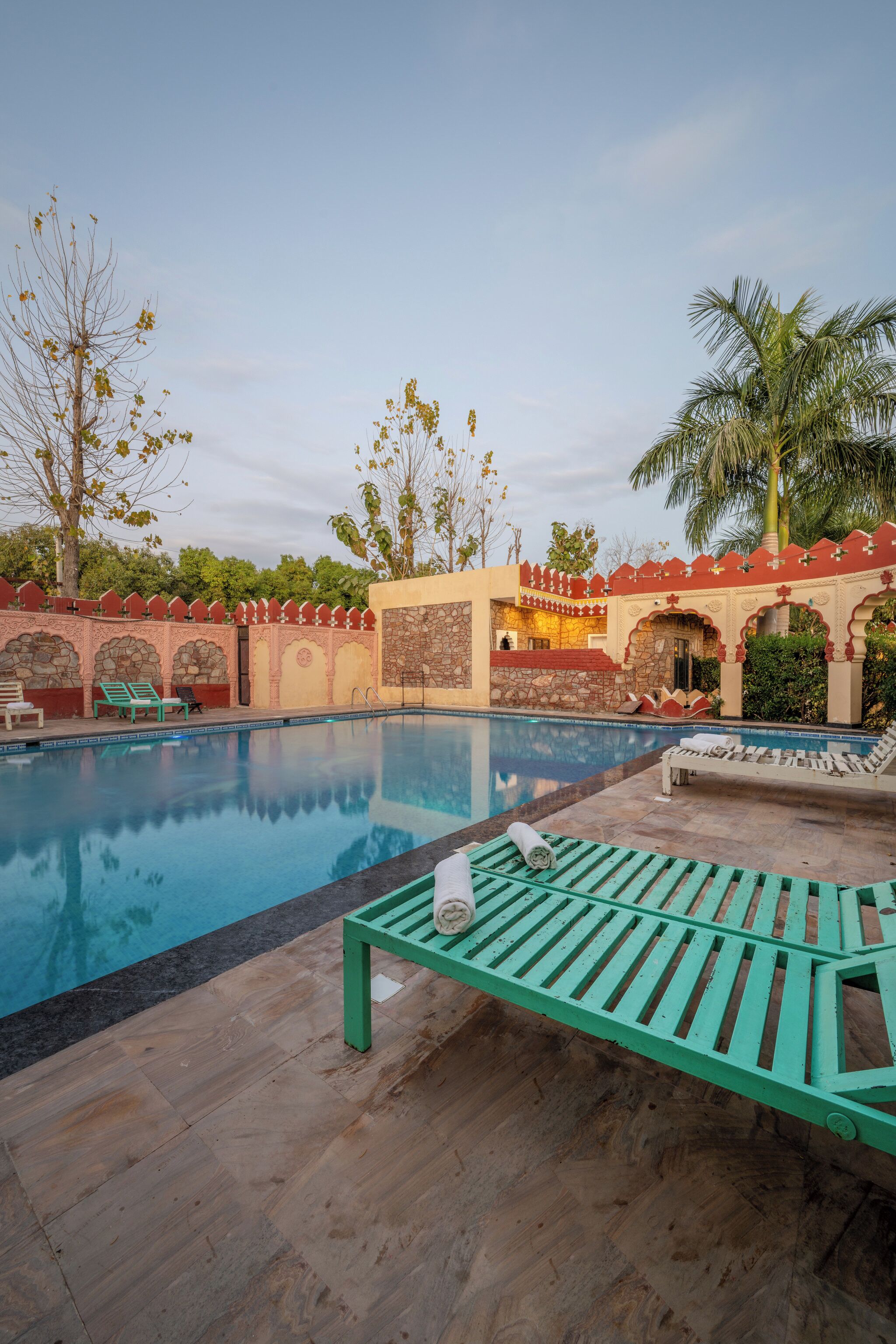 Un área de piscina con cubierta de madera, sillas de descanso y pared de piedra con arcos.
