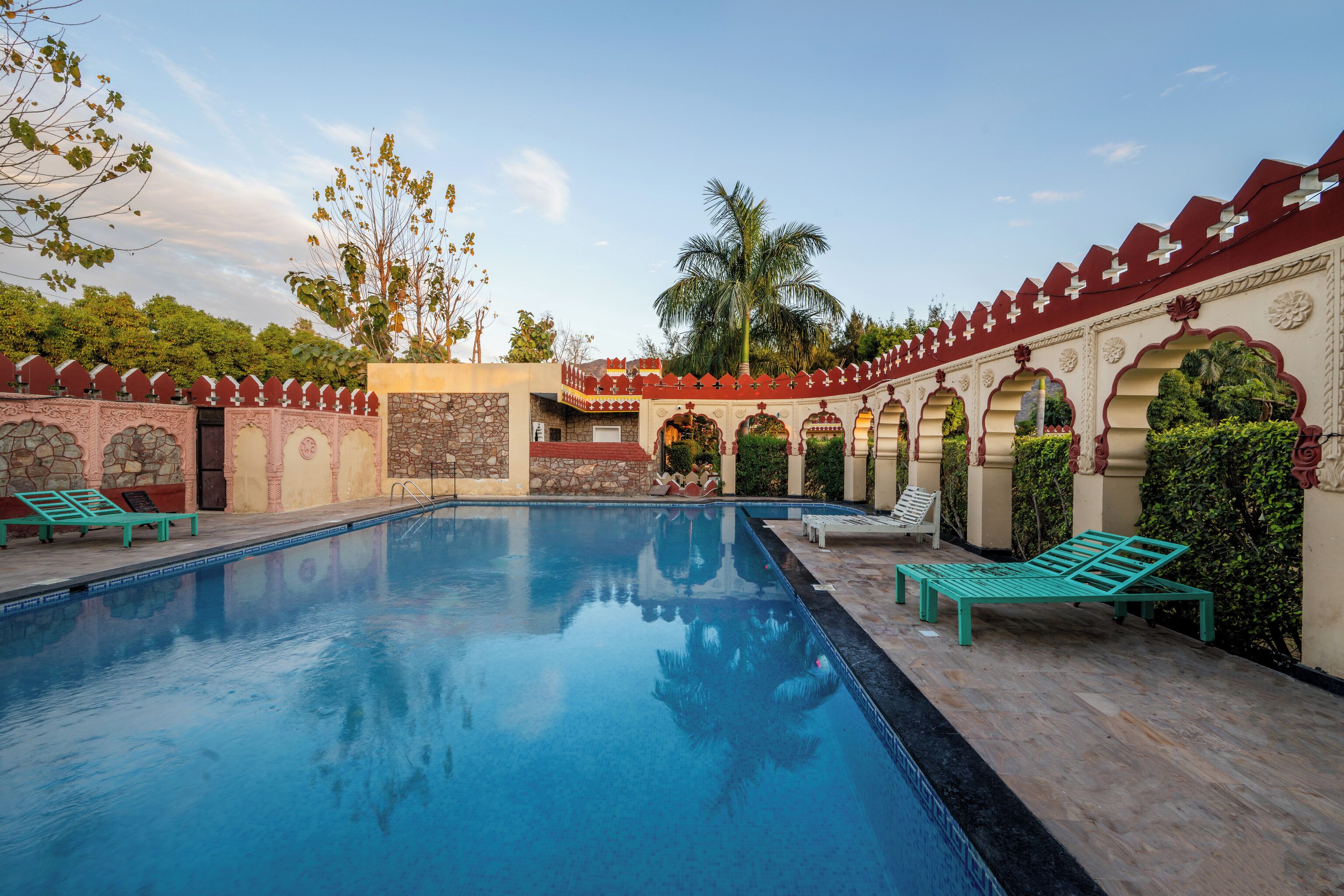 A pool area with a stone wall, benches, and a palm tree.