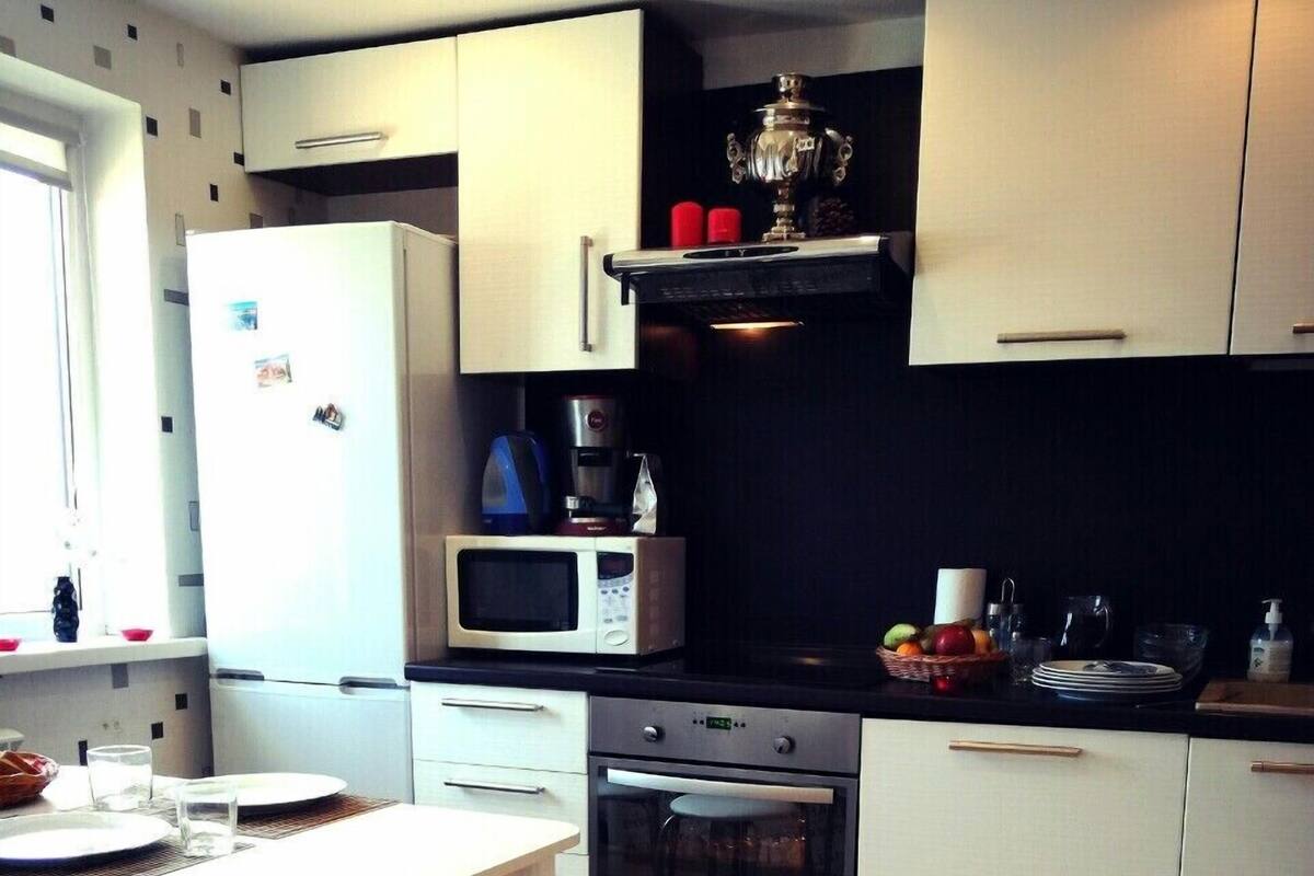 A modern kitchen with white cabinetry, a dining table with chairs, a refrigerator, a microwave, a coffee maker, and a shelf with a decorative item.