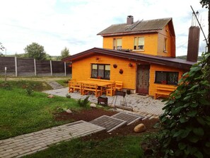 Kaksikerroksinen puutalo, jossa on terassi, jossa on puinen pöytä ja tuolit.