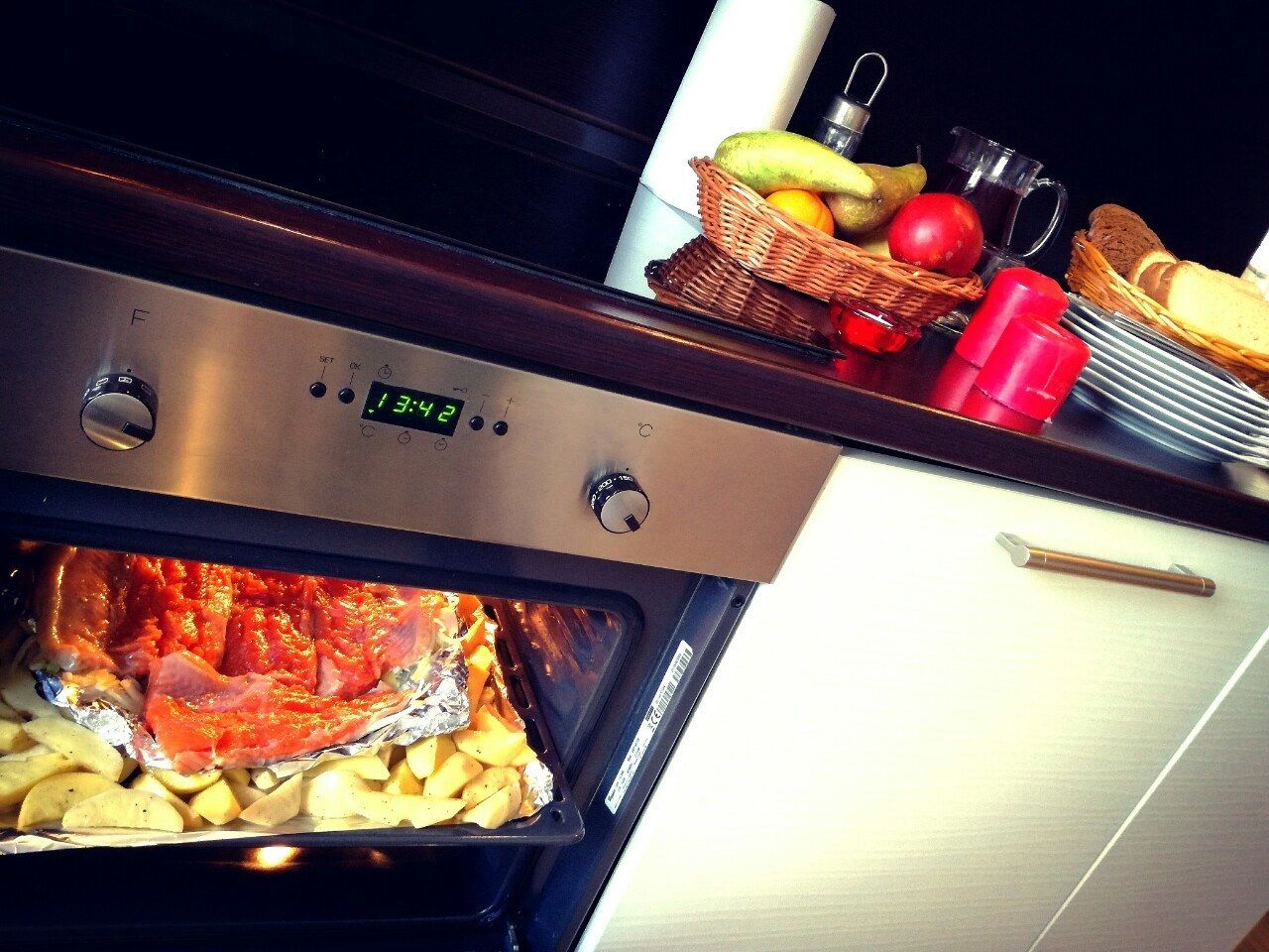 For forn amb menjar a dins, un rellotge digital i una cistada de fruita al taulell.