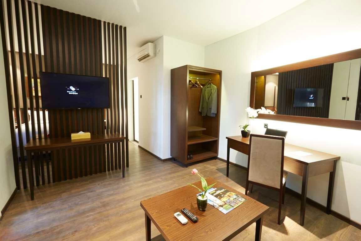 A hotel room with a TV, a desk, a chair, a wooden floor, a closet, and a mirror.