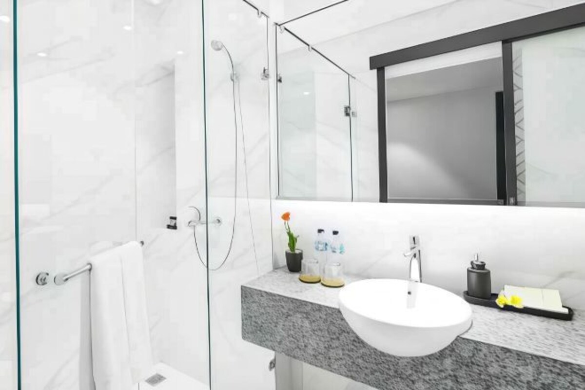 Une salle de bain moderne avec une douche à l’italienne en verre, un meuble-lavabo en marbre et un grand miroir.