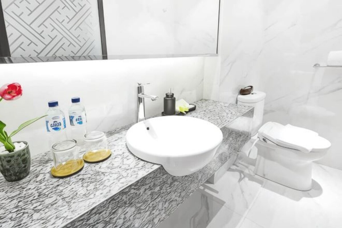 Une salle de bain avec un lavabo blanc, un plan de toilette en marbre, des toilettes et un vase avec une fleur.