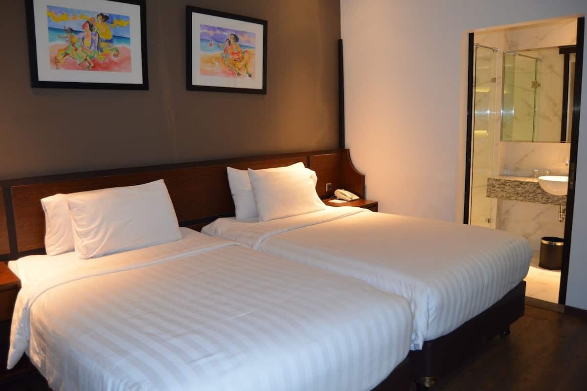 A double bed with white linens, a wooden headboard, and two framed artworks on the wall.