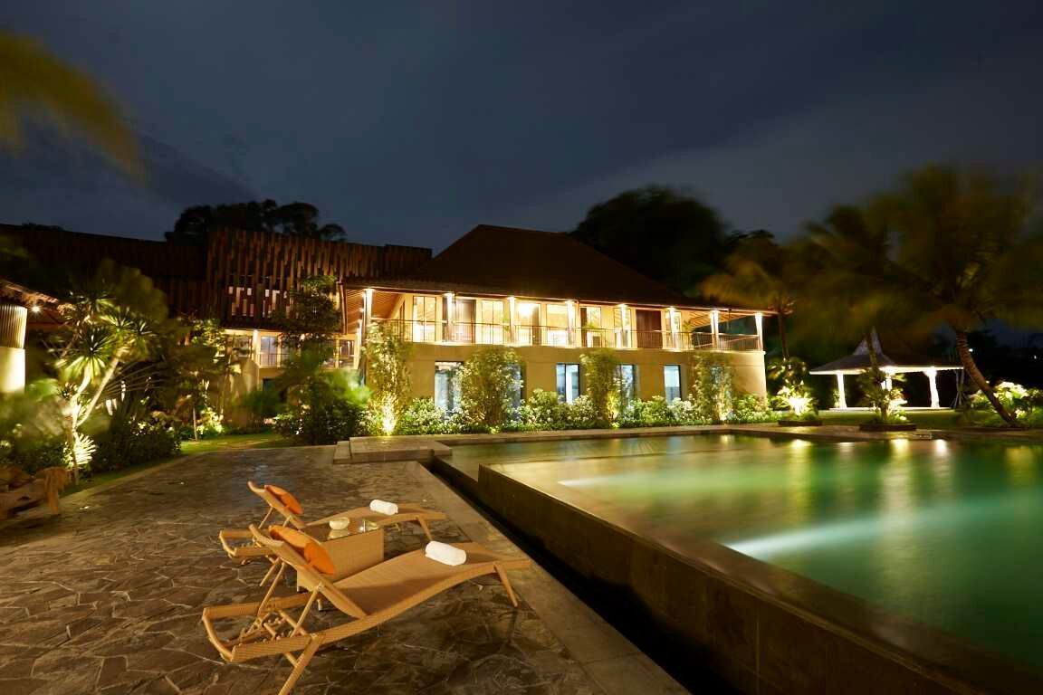 A hotel with a swimming pool, lounge chairs, and a well-lit exterior at night.