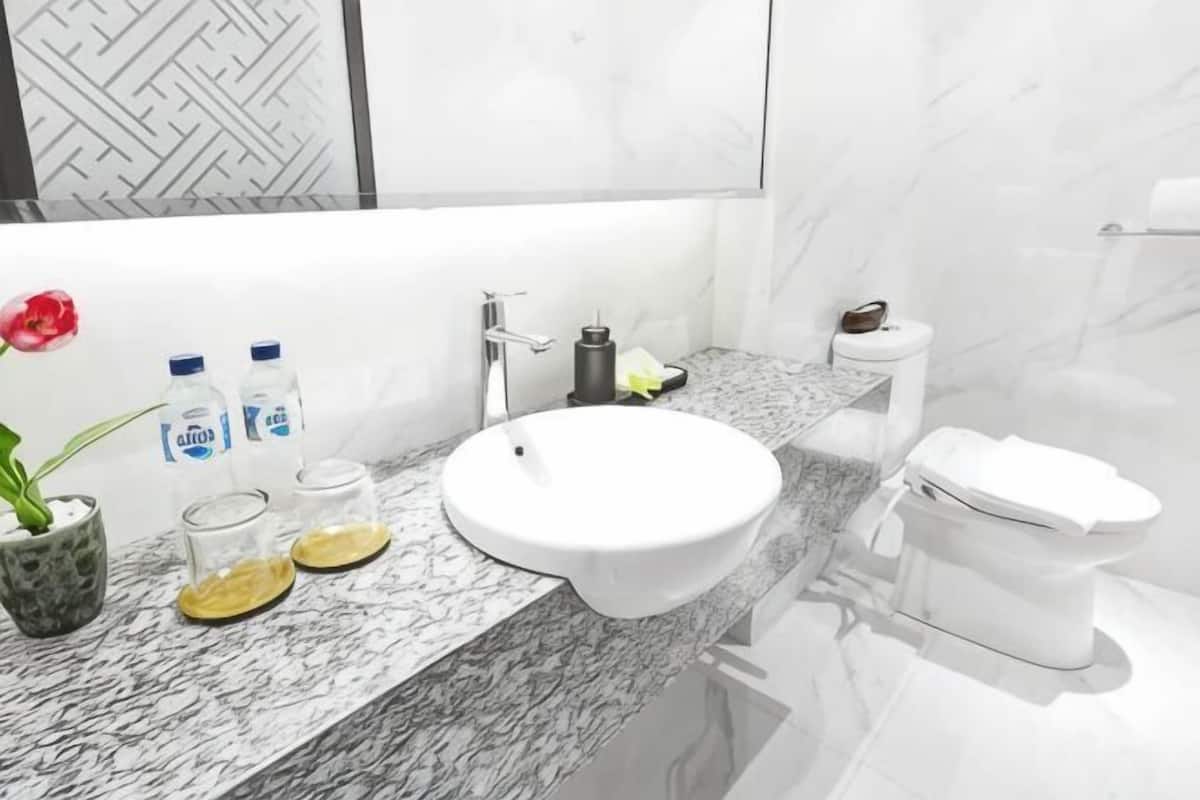 A bathroom with a white sink, marble countertop, toilet, and a vase with a flower.