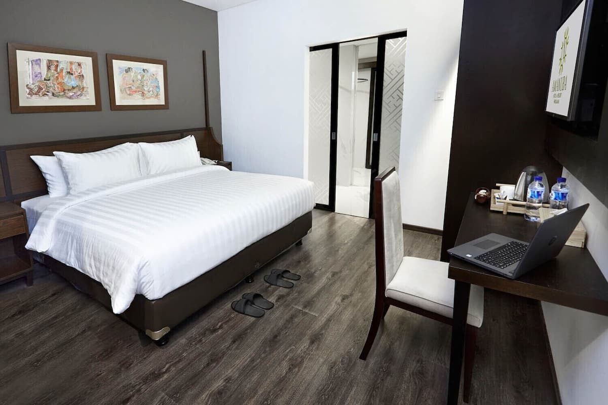 A modern hotel room with a large bed, a desk with a laptop, and a door leading to a bathroom.