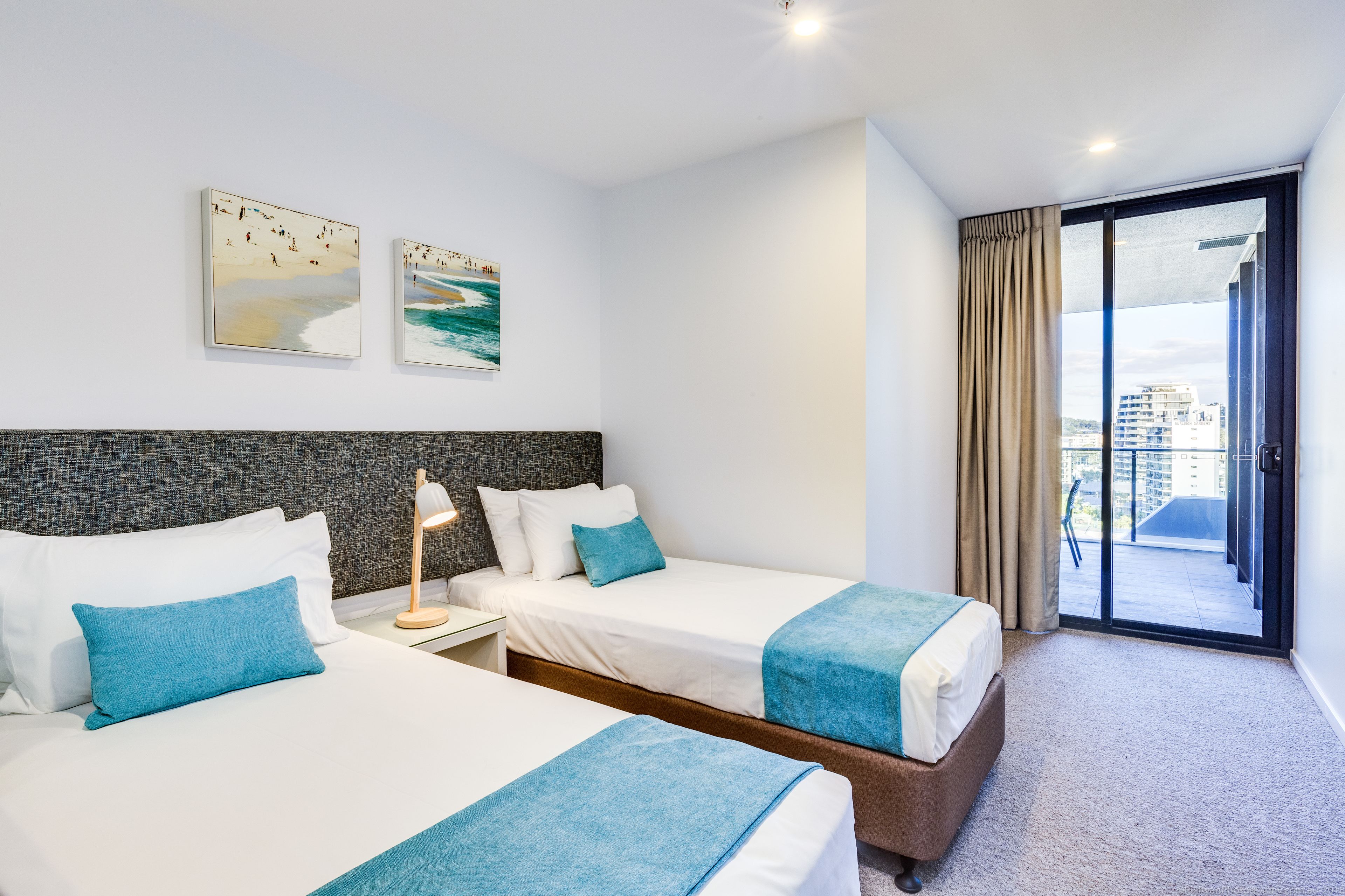 A hotel room with two beds, a large window with a view of the city, and artwork on the wall.