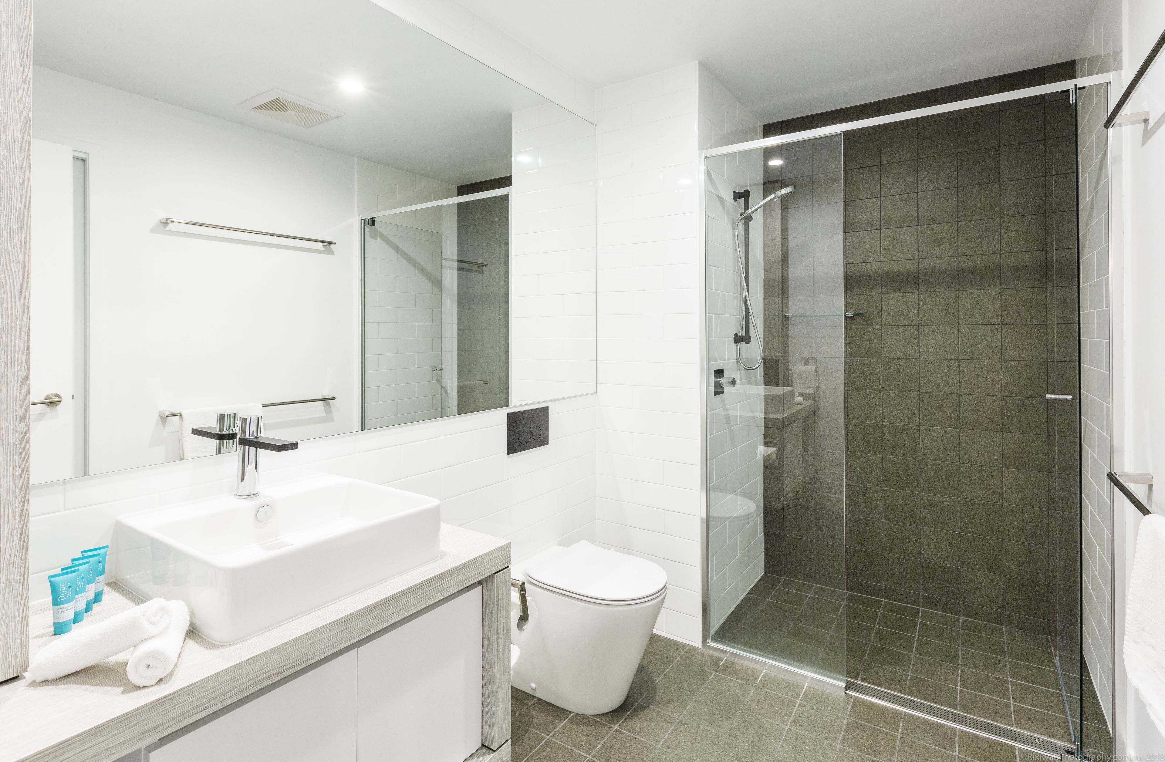 A modern bathroom with a large mirror, white sink, and a glass-enclosed shower.