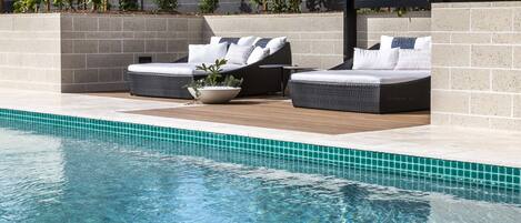 A poolside area with two wicker lounge chairs, a potted plant, and a tiled pool edge.