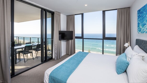 Habitación de hotel con una cama grande, televisión y balcón con vista al océano.