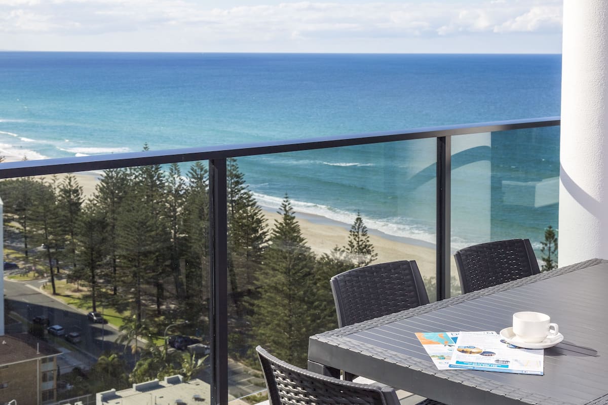 A balcony with a table and chairs overlooking a beach and ocean.