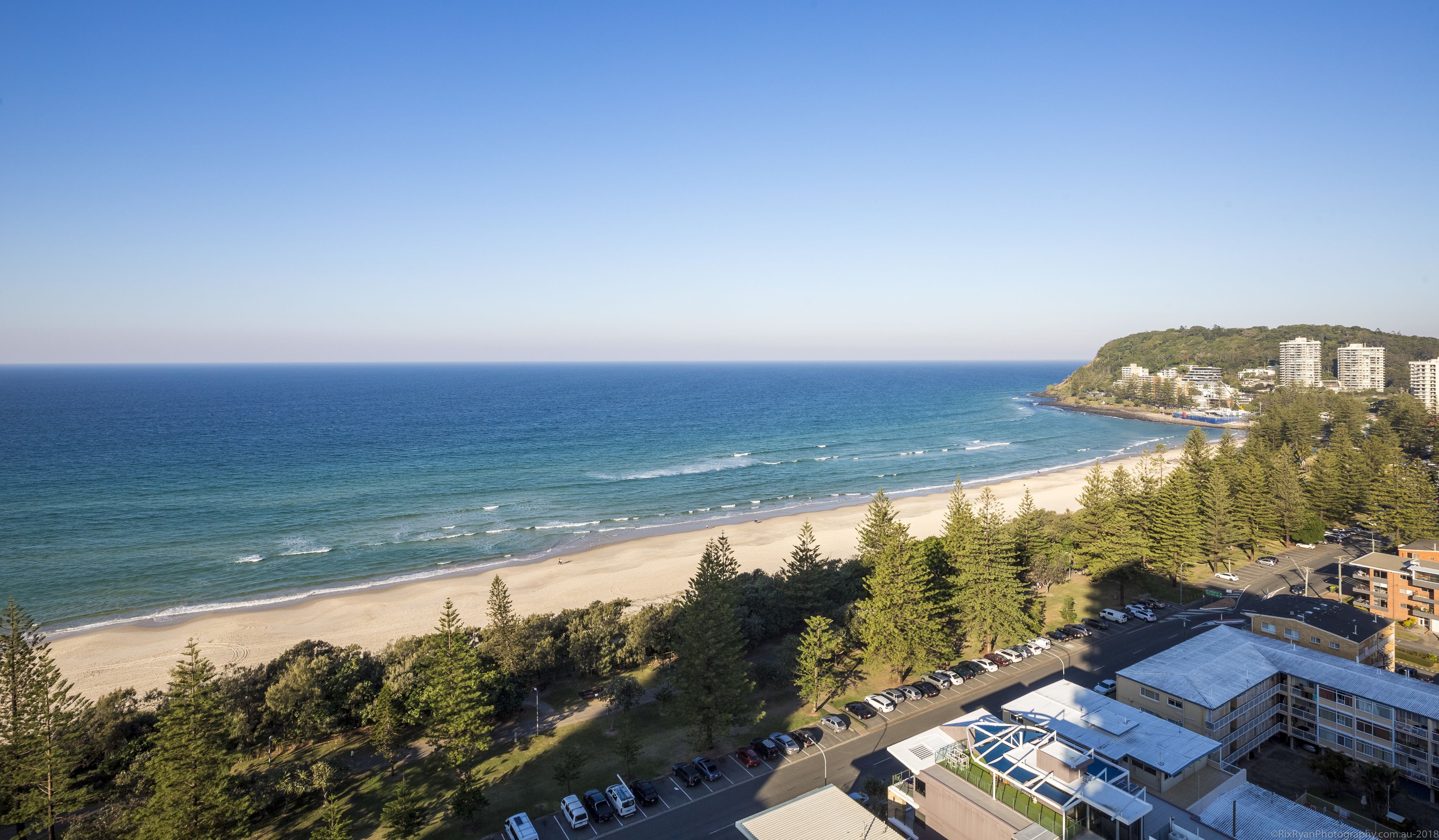 A coastal view with a beach, parking area, and buildings.