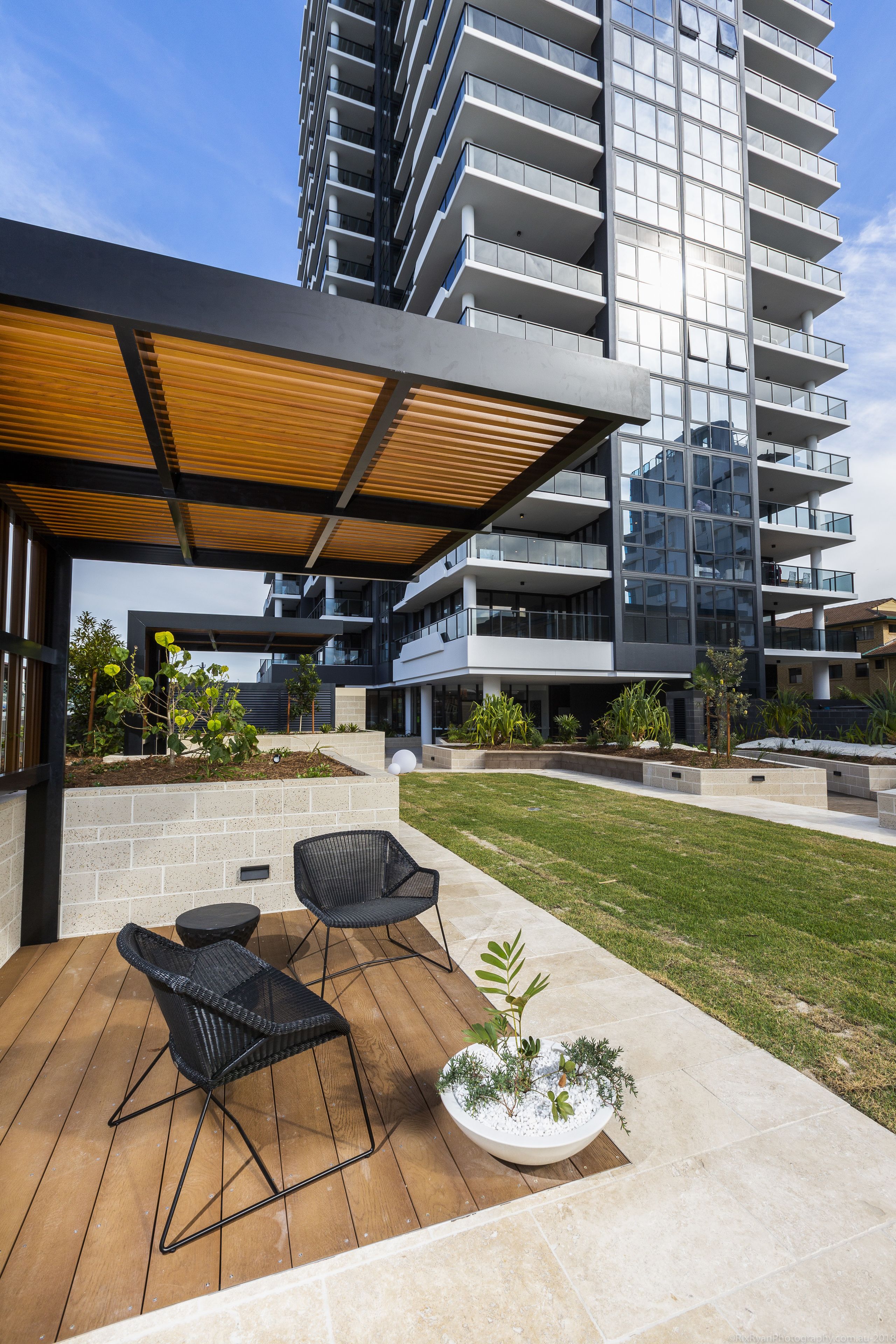 Une terrasse extérieure moderne avec un plancher en bois, des chaises en osier noir et un jardinier agrémenté de plantes vertes.