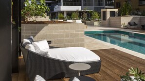 Un área de piscina moderna al aire libre con sillones de descanso y una terraza de madera.