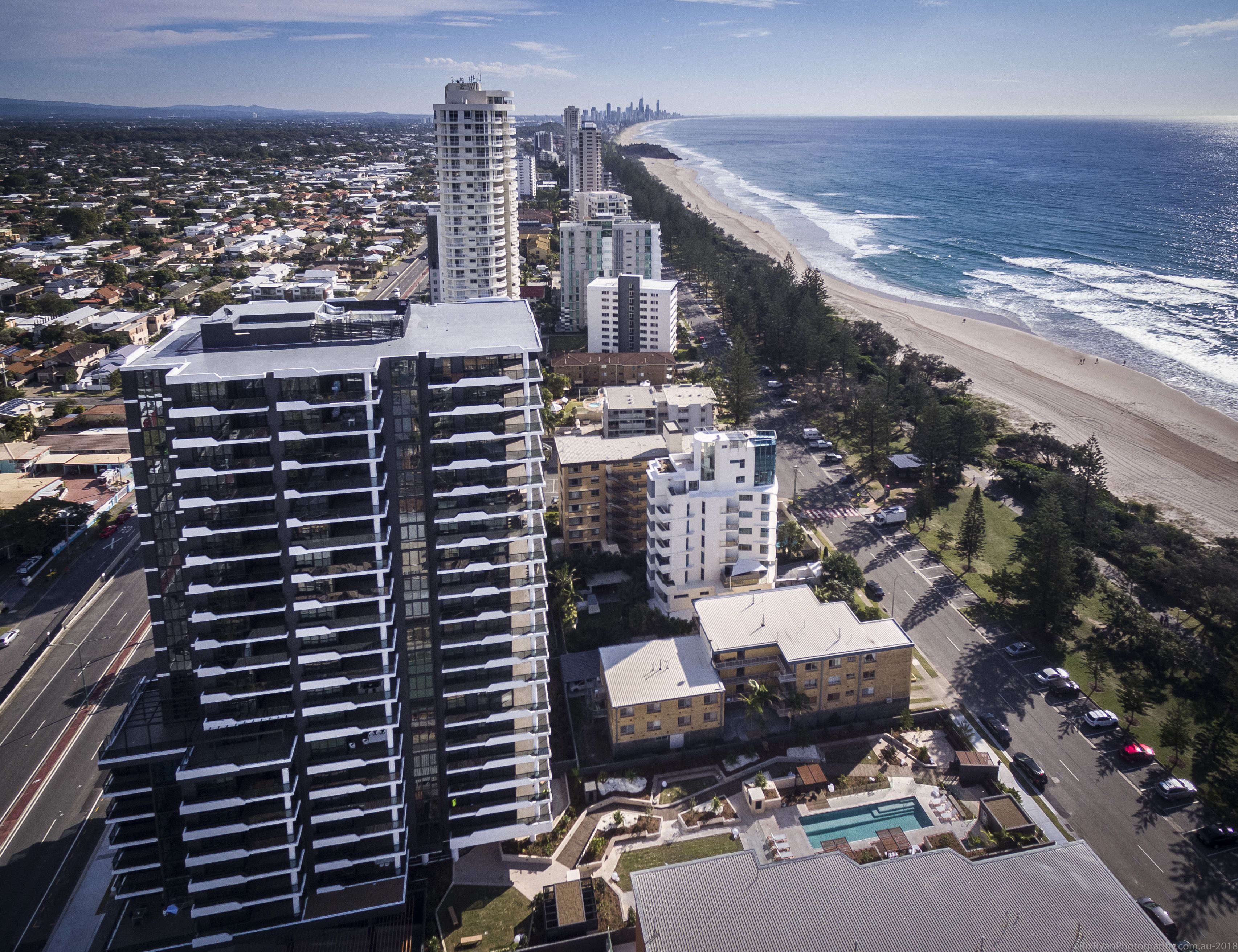 A high-rise hotel with multiple floors, a swimming pool, and a beachfront view.
