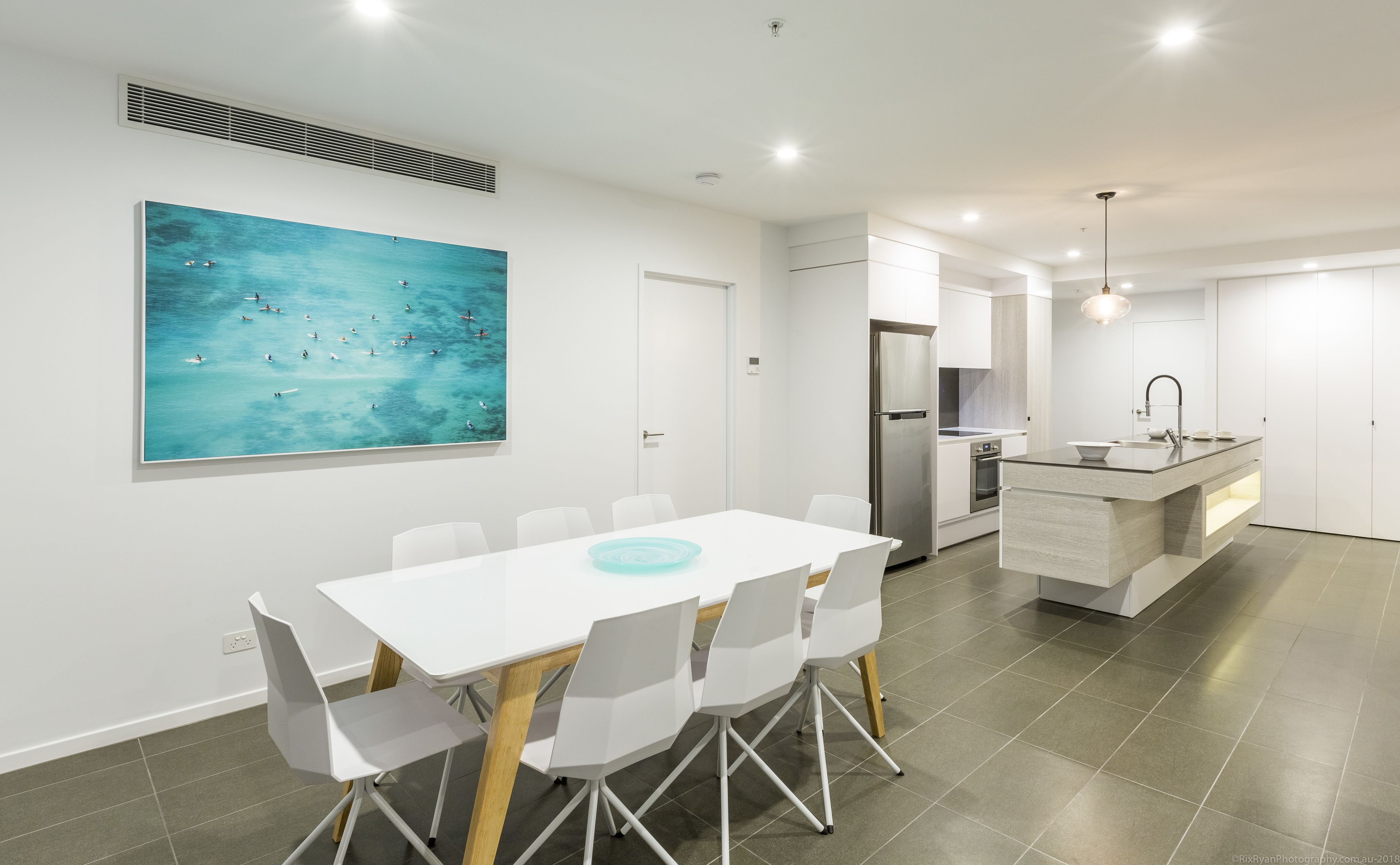 A modern kitchen with a central island, white cabinetry, and a stainless steel refrigerator.