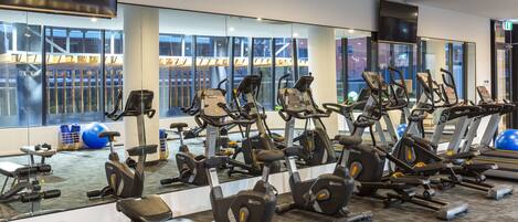 A gym with multiple exercise machines, mirrors, and large windows.
