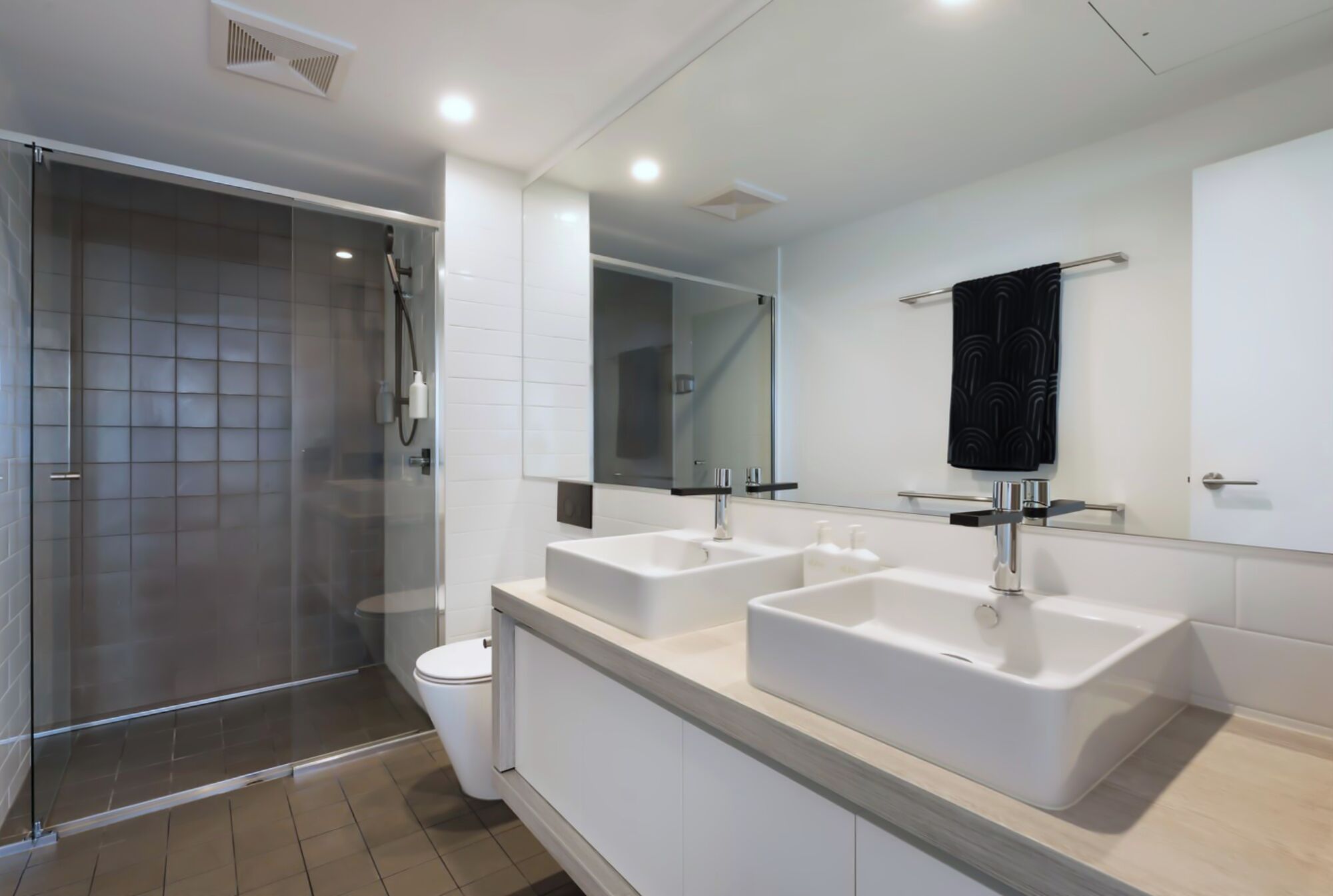 A modern bathroom with a glass-enclosed shower, two sinks, and a large mirror.