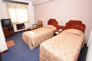 A hotel room with two single beds, a television, a desk, and a chair.
