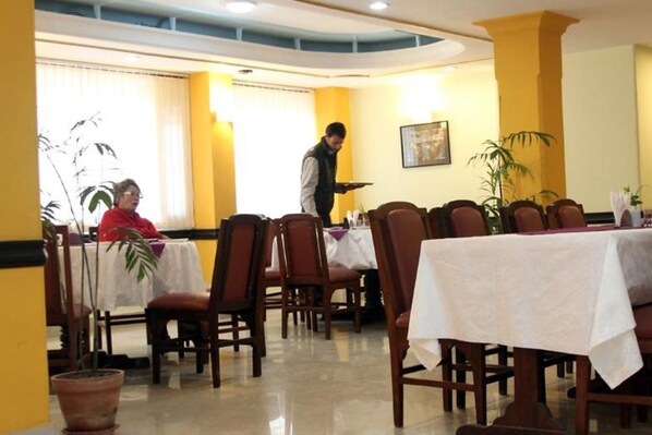 A restaurant with wooden chairs and tables, a waiter, and a customer.