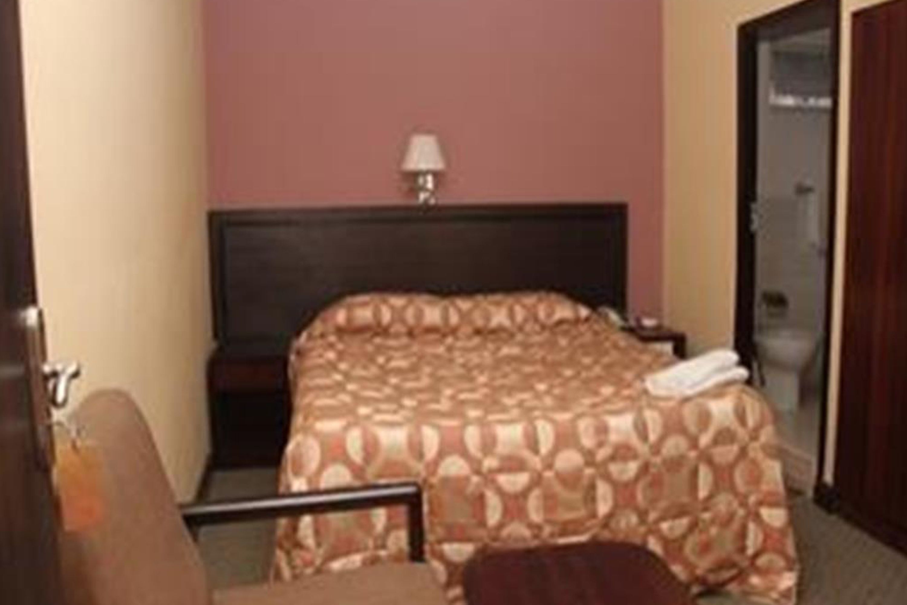 A hotel room with a bed, a nightstand, a lamp, and a chair.
