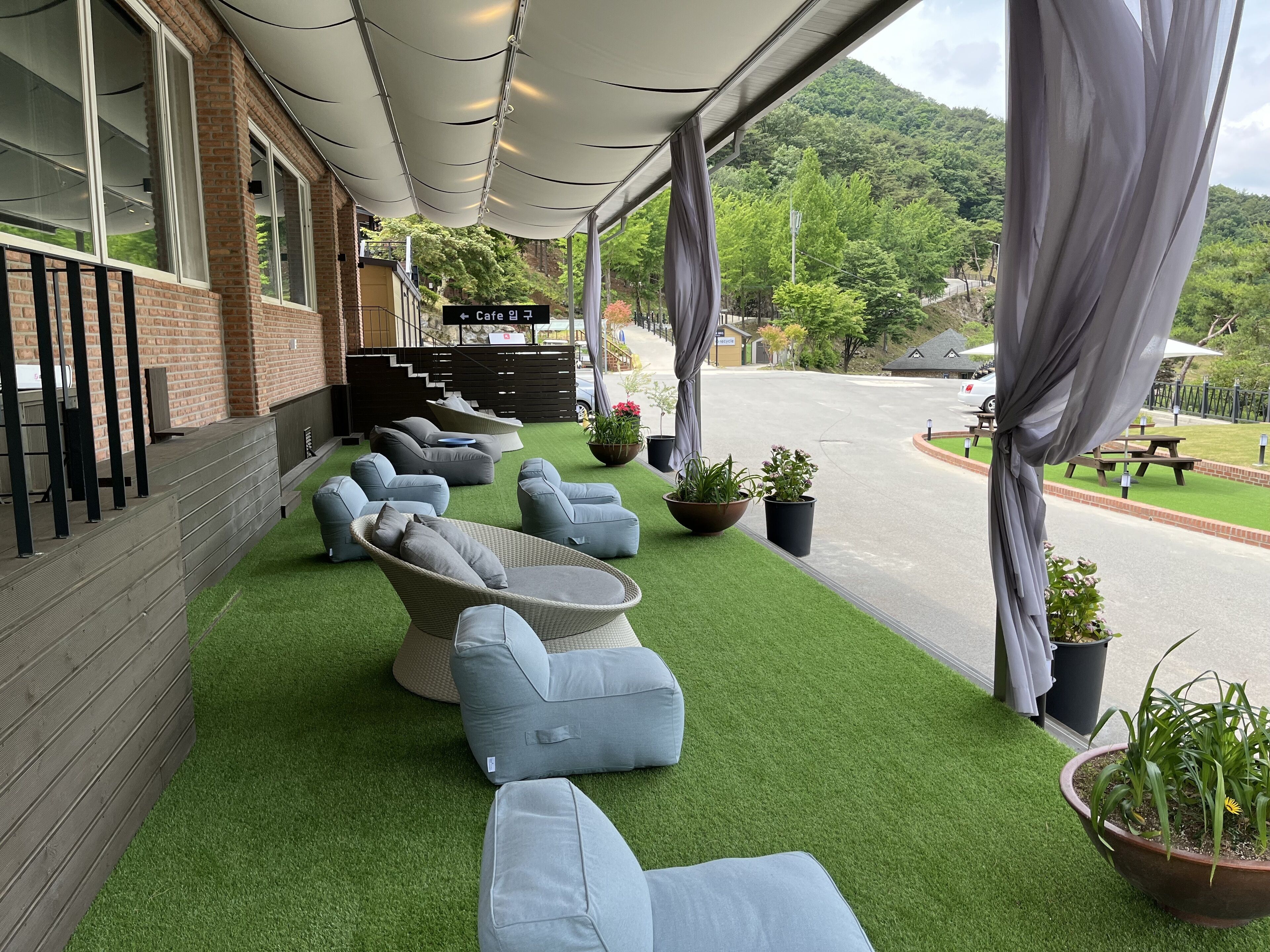 A covered outdoor seating area with artificial grass, cushioned chairs, and potted plants.