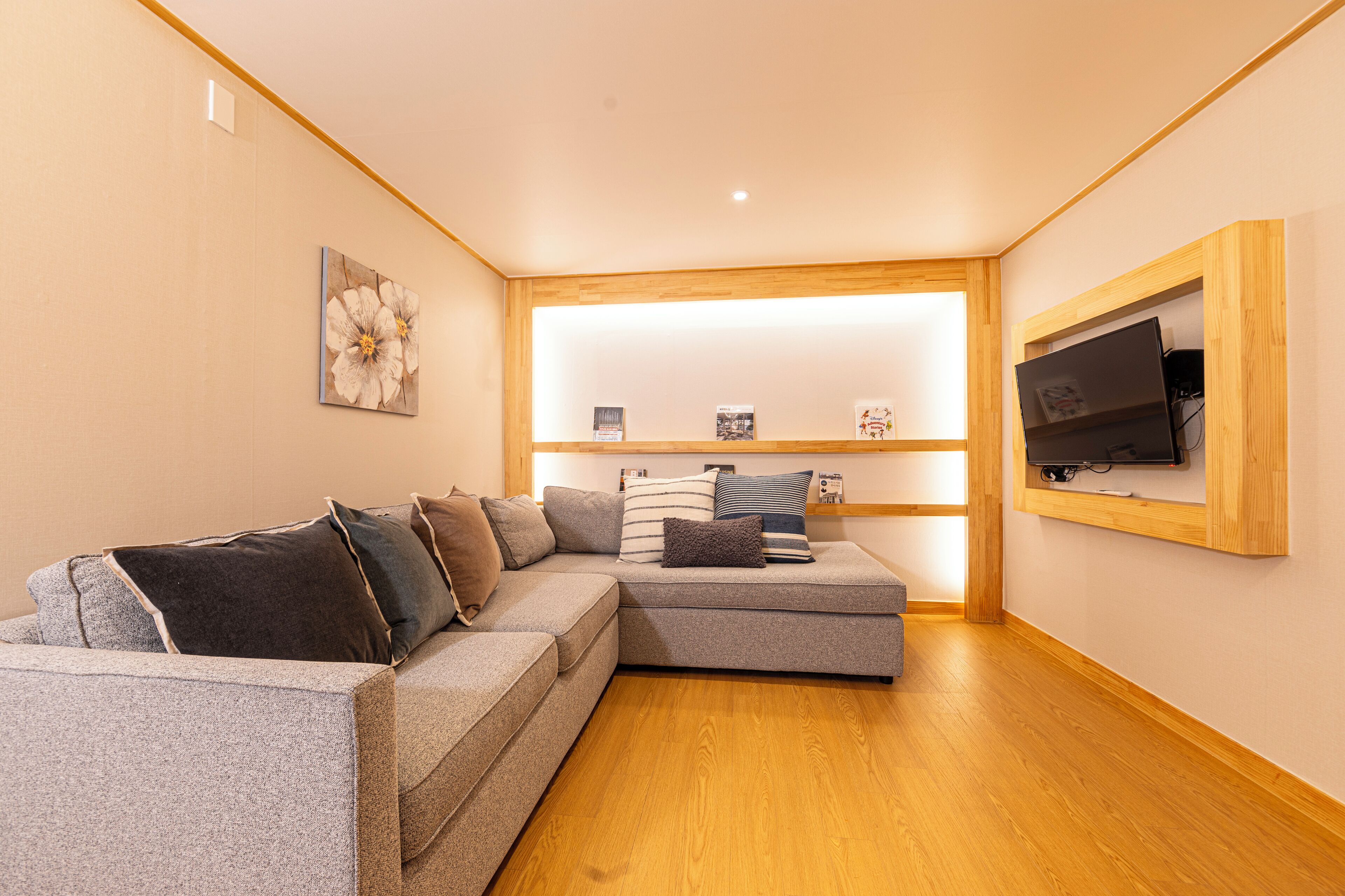 A modern living room with a grey sectional sofa, a mounted TV, and a wooden floor.