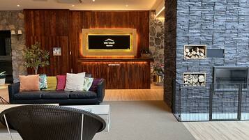 A modern reception area with a wooden wall, a stone accent wall, a mounted TV, and a seating area with a sofa and chairs.