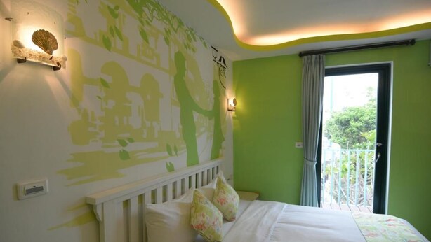 A bedroom with a bed, pillows, a wall-mounted light, a window with curtains, and a balcony. - Galilee Bed and Breakfast (Hengchun)