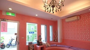 A room with a pink wall, a chandelier, a sofa, and a window with a view of a green building. - Galilee Bed and Breakfast (Hengchun)