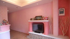 A pink-walled room with a fireplace, a small TV, and a shelf with various items. - Galilee Bed and Breakfast (Hengchun)