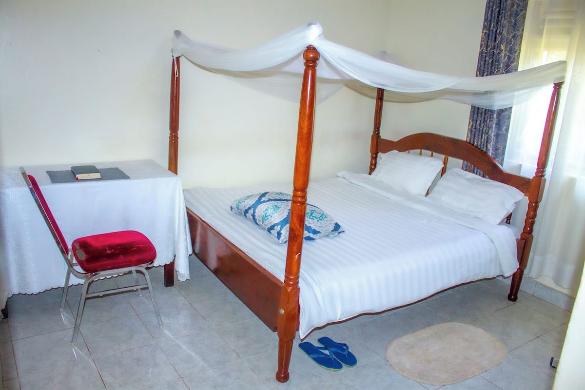 A four-poster bed with a canopy, a desk with a chair, and a small rug on the floor.