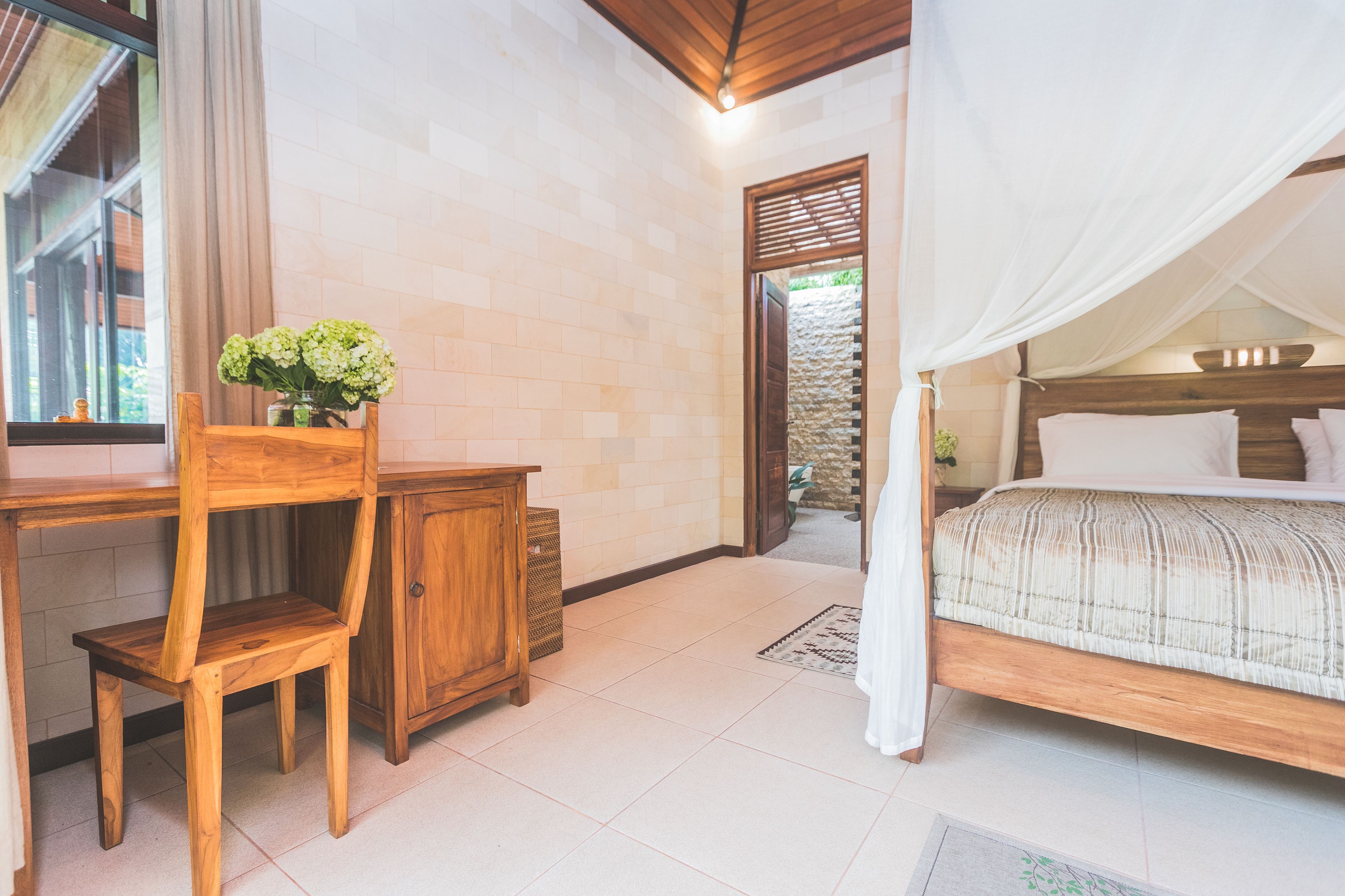 A bedroom with a bed, wooden desk, chair, and a vase of flowers.